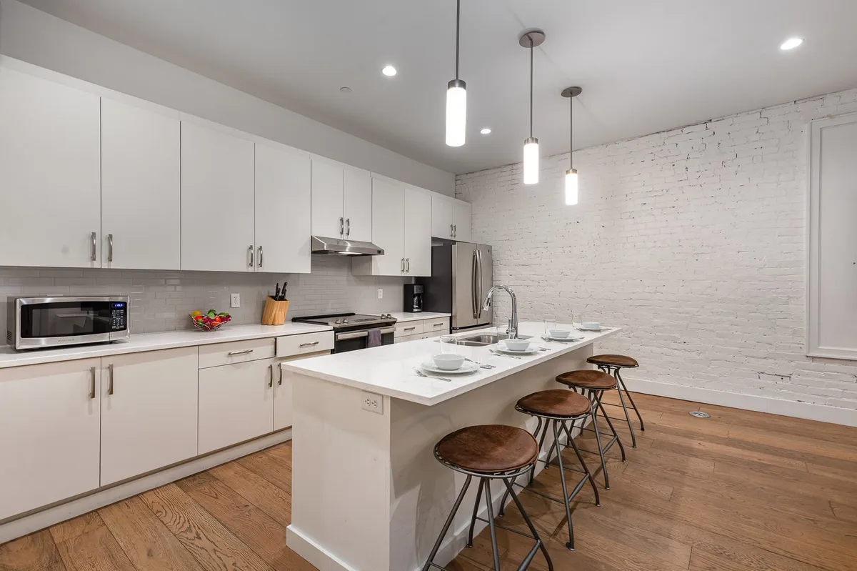 A chic, modern open lounge interior with a kitchen island, white brick wall, and stylish stools, offering a perfect spot for groups to gather before heading out. The inviting space is ideal for socializing, taking group selfies, and preparing for a night on the town.