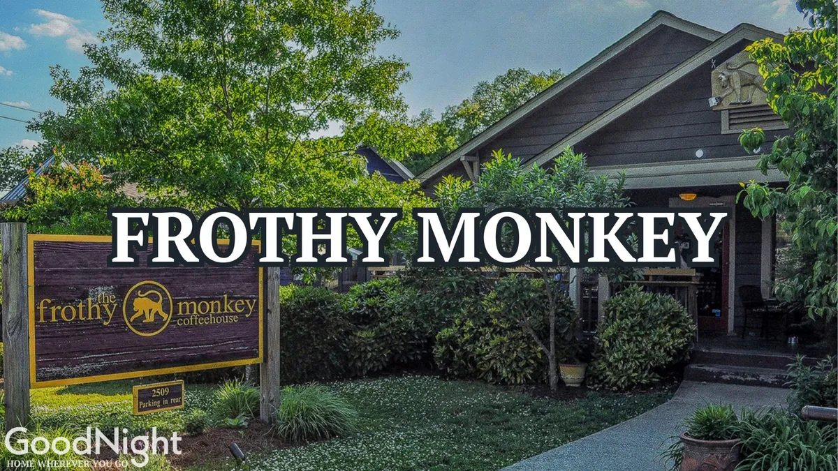 The exterior of Frothy Monkey is showcased with its inviting signage and charming architectural details, nestled among greenery. Outdoor seating and groups of people enjoying coffee contribute to an inviting, social vibe.
