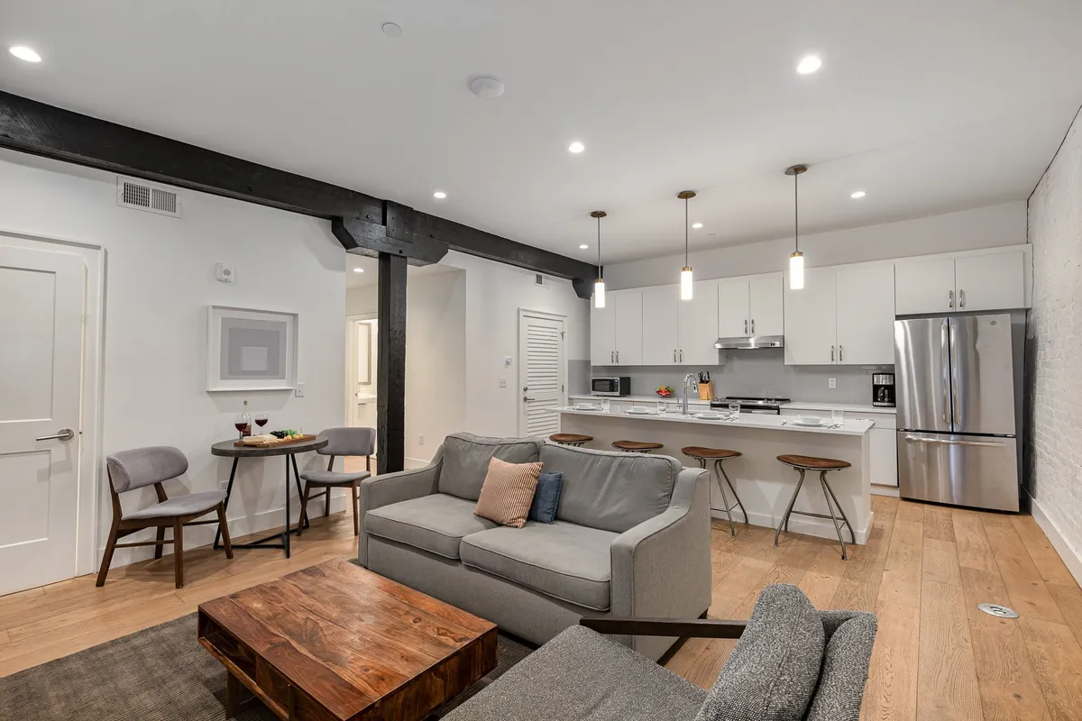 The image showcases an inviting, contemporary open-plan living space, featuring a cozy sofa, a stylish kitchen island, a warm wooden coffee table, and a welcoming dining area—perfect for gathering with friends or relaxing after a day out in Nashville. The soft lighting and modern touches create a comfortable, sociable atmosphere.