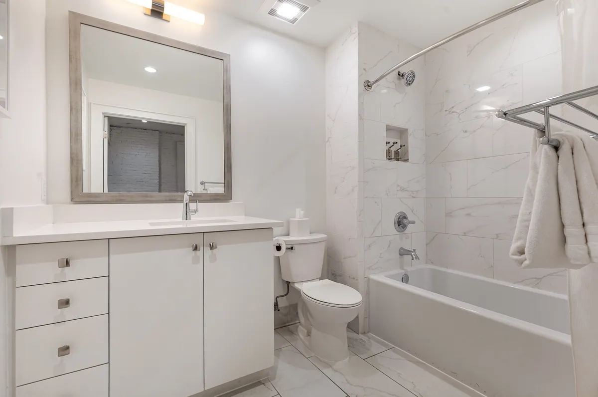 This image features a modern bathroom with a large mirror above a single vanity, a sleek sink, a well-lit shower area, and a separate bathtub. The clean lines, neutral tones, and uncluttered surfaces create a soothing, spa-like atmosphere ideal for both pre-event preparations and relaxing post-show routines.