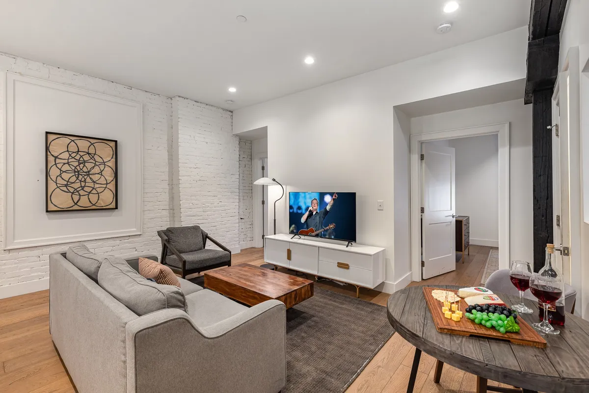 A stylish living room with a comfortable sofa, coffee table with snacks, television, artwork, and an adjacent snack table. The space exudes a cozy, social vibe ideal for entertaining guests or enjoying a relaxed evening together.